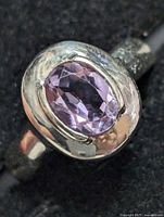 Close-up shot of the silver ring with a faceted oval amethyst gemstone from a slight angle showing the stone's detailing and bezel setting.