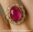 Close-up of silver ring showing large oval cabochon ruby center stone with surrounding gold bezel and detailed silver floral motif.