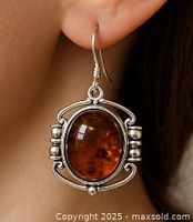 Close-up photo of an amber and silver earring being worn on ear showing the oval amber stone and silver frame design