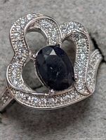 Close-up image showing the front view of the sterling silver ring with a large oval blue sapphire and numerous small cubic zirconia stones around it.