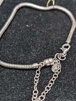 Close-up photo of the sterling silver snake chain bracelet showing clasp and safety chain with a Pandora style tag.