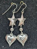 Pair of sterling silver dangle earrings lying on a dark surface, showing the front side with star, sphere, and heart elements