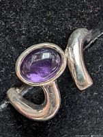 Close-up of silver ring with oval cabochon amethyst stone on a black background.