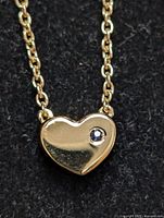 Close-up of heart-shaped pendant showing sapphire stone and silver finish on black background.