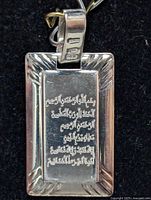 Close-up of rectangular sterling silver pendant with Arabic script engraving and hallmark stamps on bail.