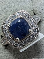 Top-down view of ring on gray jewelry pad showing central sapphire and zirconia halo