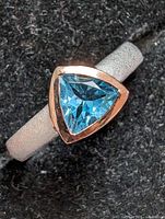 Close-up showing the triangular trillion cut blue topaz set in a bezel setting on a matte finish sterling silver band.