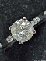 Close-up front view of sterling silver ring with 1.56 carat round moissanite center stone and accent stones on band