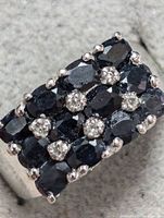 Close-up front view of sterling silver ring showing three rows of oval deep blue sapphires with white accent stones