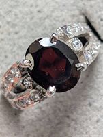 Close-up photo of the sterling silver ring featuring a large oval garnet gemstone and clear accent stones on the band.