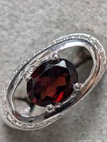 Close-up photo of the sterling silver ring showing the faceted oval garnet gemstone in the center with an open oval frame around it and silver prongs holding the gem.
