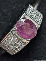 Close-up front angle of sterling silver ring with oval faceted ruby and pave-set small clear stones on band sides.