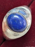Top view of sterling silver ring with prominent oval lapis lazuli cabochon gemstone against a red velvet background.