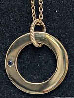 Close-up image of sterling silver necklace pendant showing circular design with a small blue stone embedded and the textured loop connecting it to the chain.
