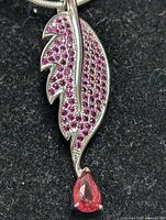 Close-up photo of a leaf-shaped sterling silver pendant adorned with small pink stones and a pear-shaped pink gemstone hanging at the tip, on a silver chain.