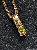 Close-up image of yellow diamond pendant set in sterling silver with medium link chain on dark fabric background.