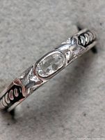 Close-up front and side view of sterling silver ring with clear oval gemstone and engraved decorative band.