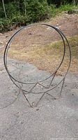 Full view of round metal firewood holder standing on pavement