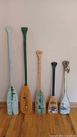 Front view of five decorated paddles leaning against wall