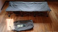 Cot fully assembled on hardwood floor with carry bag in front