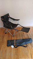 Full view of folding camping chair with attached footrest and carry bag on floor