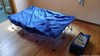 Assembled collapsible bed frame with blue cover and rolling bag