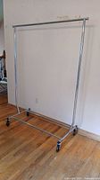 Full view of chrome garment rack on hardwood floor showing casters and hanging bar