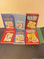 Front view of six hardcover books from Diary of a Wimpy Kid and Dork Diaries series