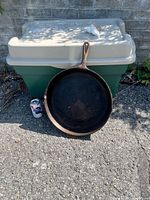 Front view of large cast iron skillet leaning against bin for scale