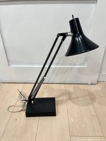 Side view of adjustable black Luxo desk lamp showing entire lamp and cord