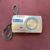 Front view showing Olympus Stylus 740 branding, lens, flash, 7.1 MP marking, wrist strap