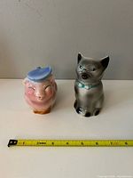 Pig and cat ceramic creamers side by side with ruler for scale