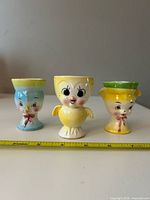 Front view of all three anthropomorphic ceramic egg cups with measuring tape