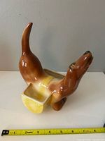 Side view of ceramic dachshund showing brown glaze, yellow compartment, tape measure indicating length