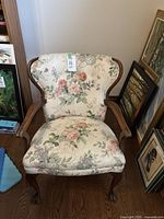 Front view of the vintage floral patterned fabric armchair showing the full seat, backrest and wooden arms and legs.