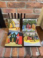 Four canvas prints arranged on brick fireplace mantle showing colorful houses and natural scenes