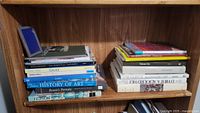 Wide shot showing two stacks of art books on a wooden shelf including titles on History of Art, Renoir, Gaudi, and more.