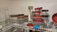 Shelf view showing 4 glass canisters with wooden lids, glass bottle, plastic containers with lids.
