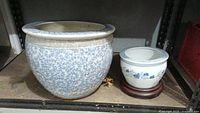 Both ceramic pots on a shelf showing size difference and condition including crack on larger pot