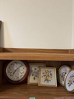 The full shelf with the clock and four floral needlepoint frames arranged next to it