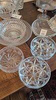 Photo of six cut crystal bowls on wooden surface with labels and price tags, showing star and diamond cut patterns, one marked Clarenbridge