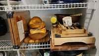 Photo of three new bamboo cutting boards still in packaging, long wooden bowl with three matching smaller bowls, round salad bowl, wooden carving board with carving set, bread slicer, and fat cup displayed on white shelving.