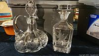 Two crystal decanters, one round with handle and one rectangular with etched floral and bird design.