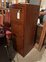 Front view of the medium wood tone 4 drawer filing cabinet with lock on top drawer and tag attached.