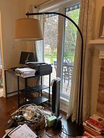 Floor lamp next to window, showing black metal arching frame and beige fabric shade over circular base.