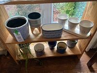 Wide view of the wooden shelf with all ceramic flower pots arranged showing variety of shapes and patterns.