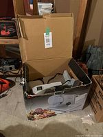 Open cardboard box containing the electric food slicer visible inside, partial view showing slicer tray and blade cover.