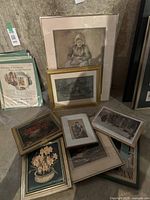 Overview of nine framed prints stacked and displayed against wall showing variety of subjects and frame styles.