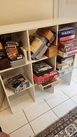 Photo showing shelving unit filled with boxed board games including Sequence, Checkers, Monopoly, and puzzles of various sizes stacked inside the shelves.