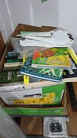 Box filled with assorted gardening books and a pair of white gloves on top.